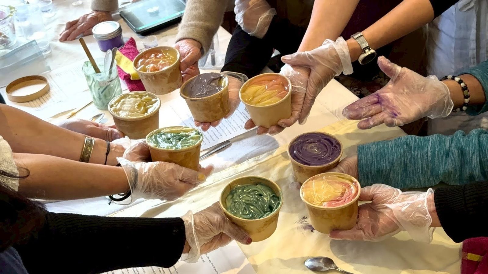 Hands holding cups of freshly made colourful soap over the workshop table